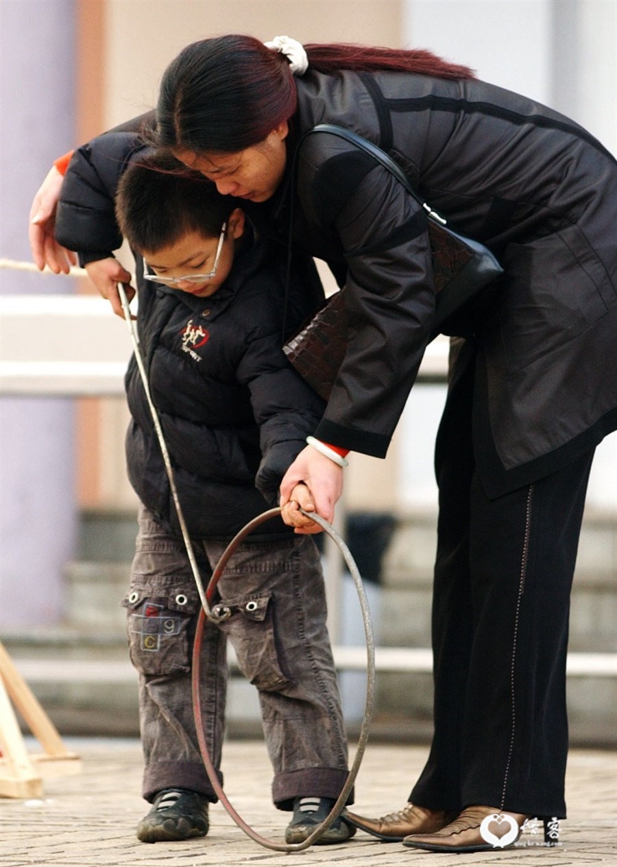 2004年11月27日,一位女士正在教儿子玩滚铁环游戏。