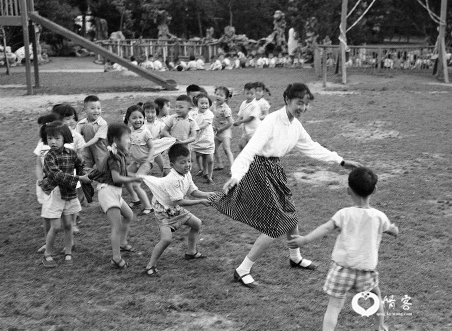 1959年,上海市一个幼儿园的草坪上,孩子们在阿姨的带领下作“老鹰捉小鸡”游戏。