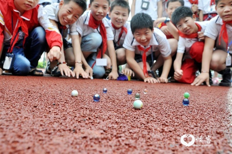 2015年5月27日,在江西省万载县第一小学,孩子们在“寻找父母儿时的老游戏”迎“六一”活动中玩打弹珠。